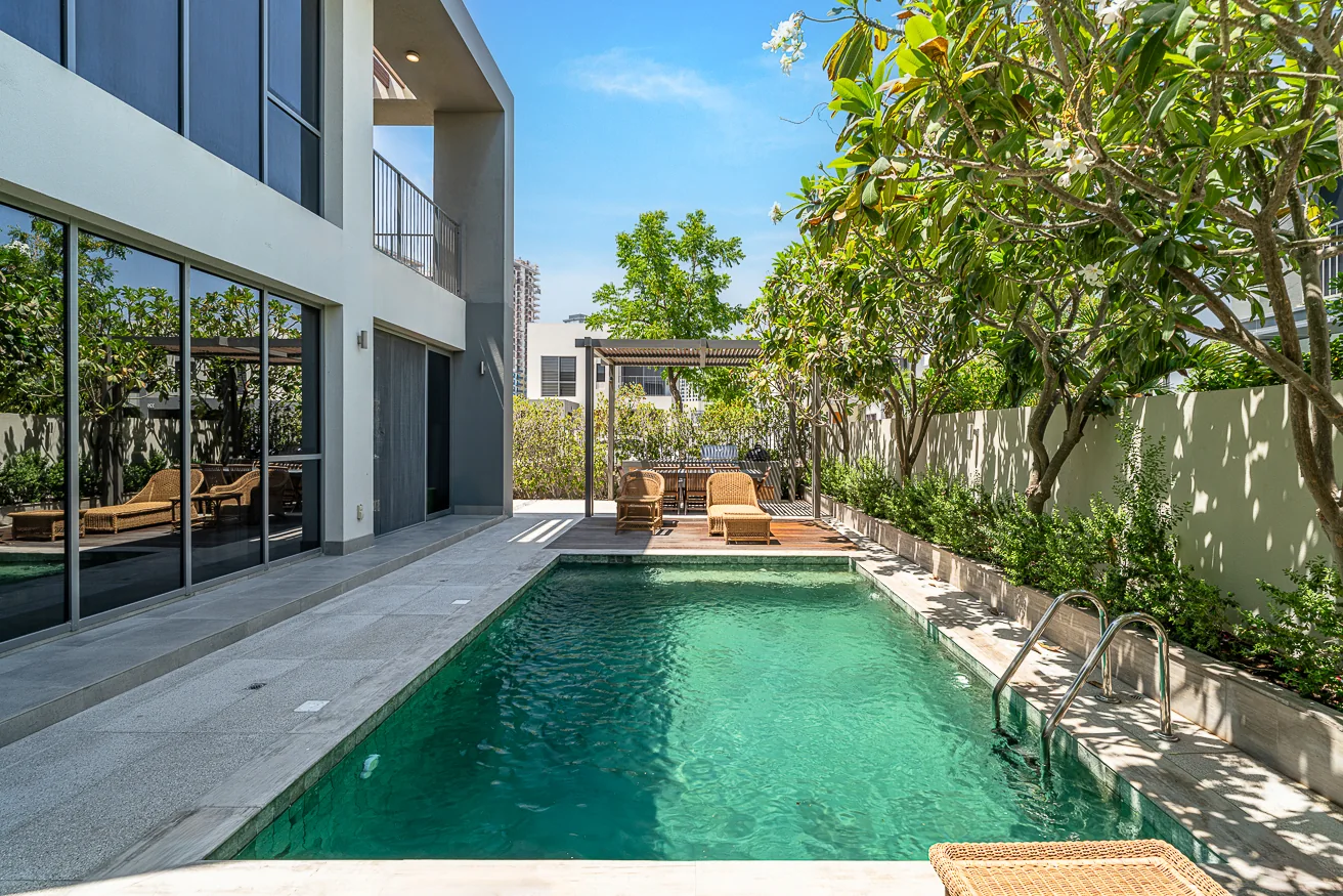 Private pool running beside the villa, with mature planting and a timber deck